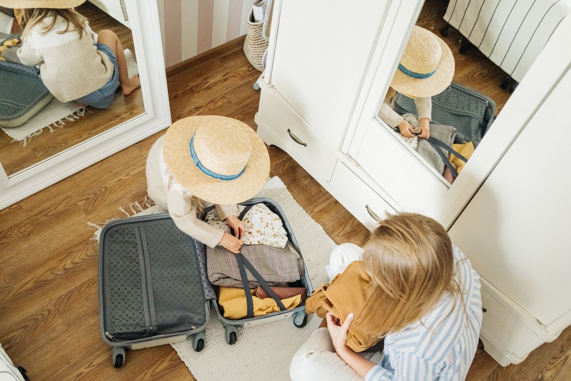 A woman and child arranging clothes in an open suitcase.