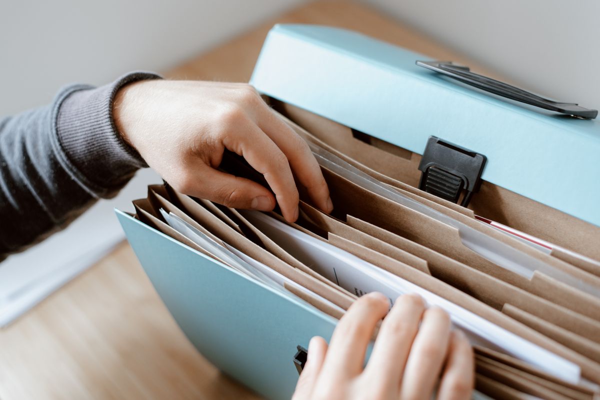 Hands sorting papers in a blue document folder.