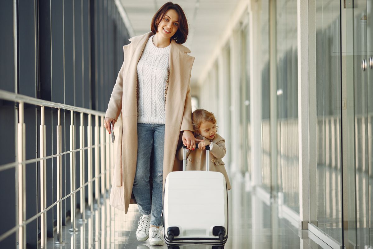 A woman and child walking through an airport with a suitcase.
