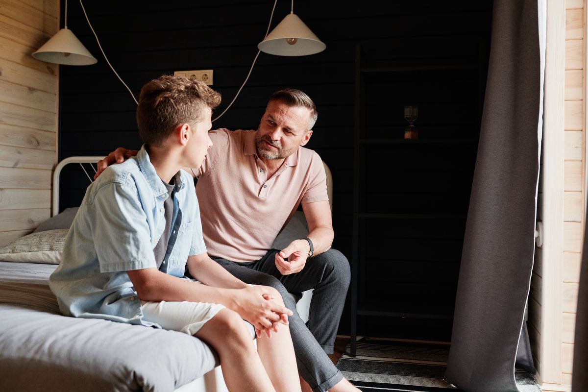 An adult and teenager talking in a bedroom.