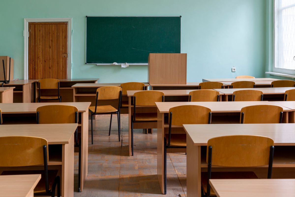 Empty classroom desks facing a green chalkboard.