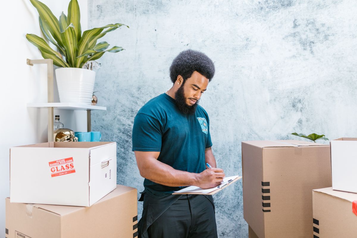 A mover checking a clipboard beside stacked boxes.