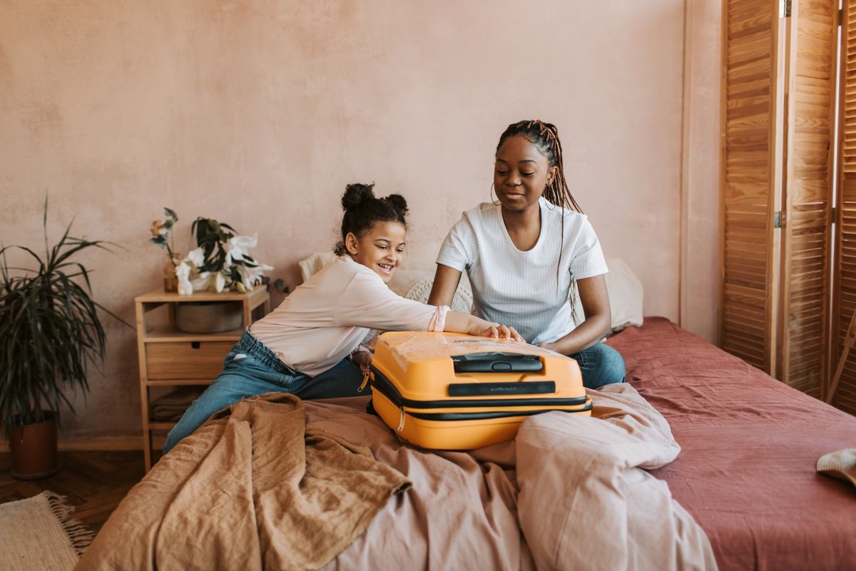 A woman and child beside a suitcase at home.