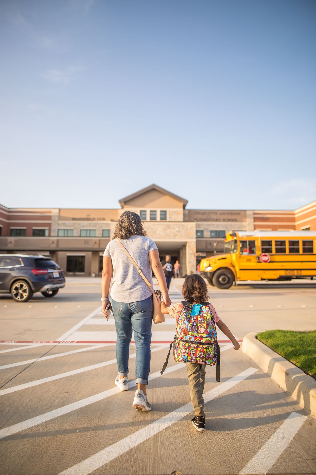 An adult and child with a backpack walking towards a school.