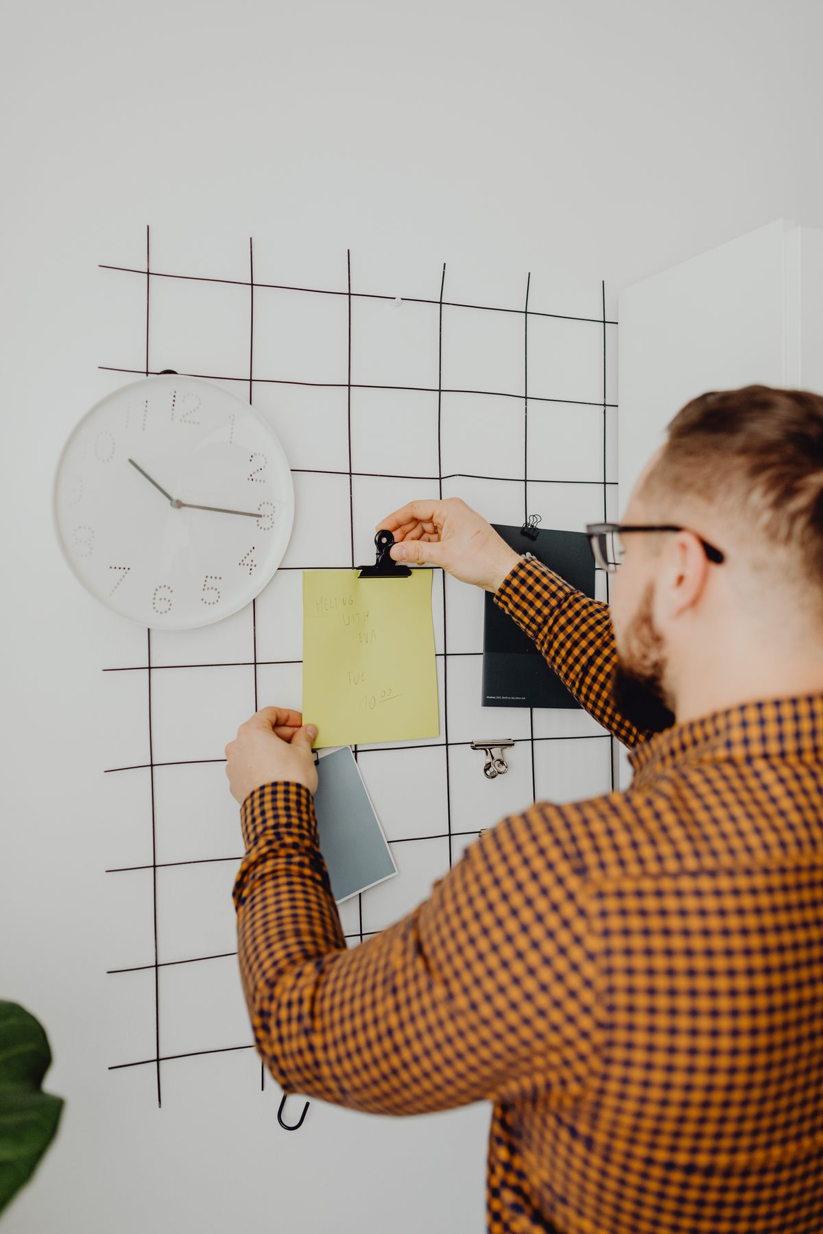A person pinning a note to a wall organiser beside a clock.
