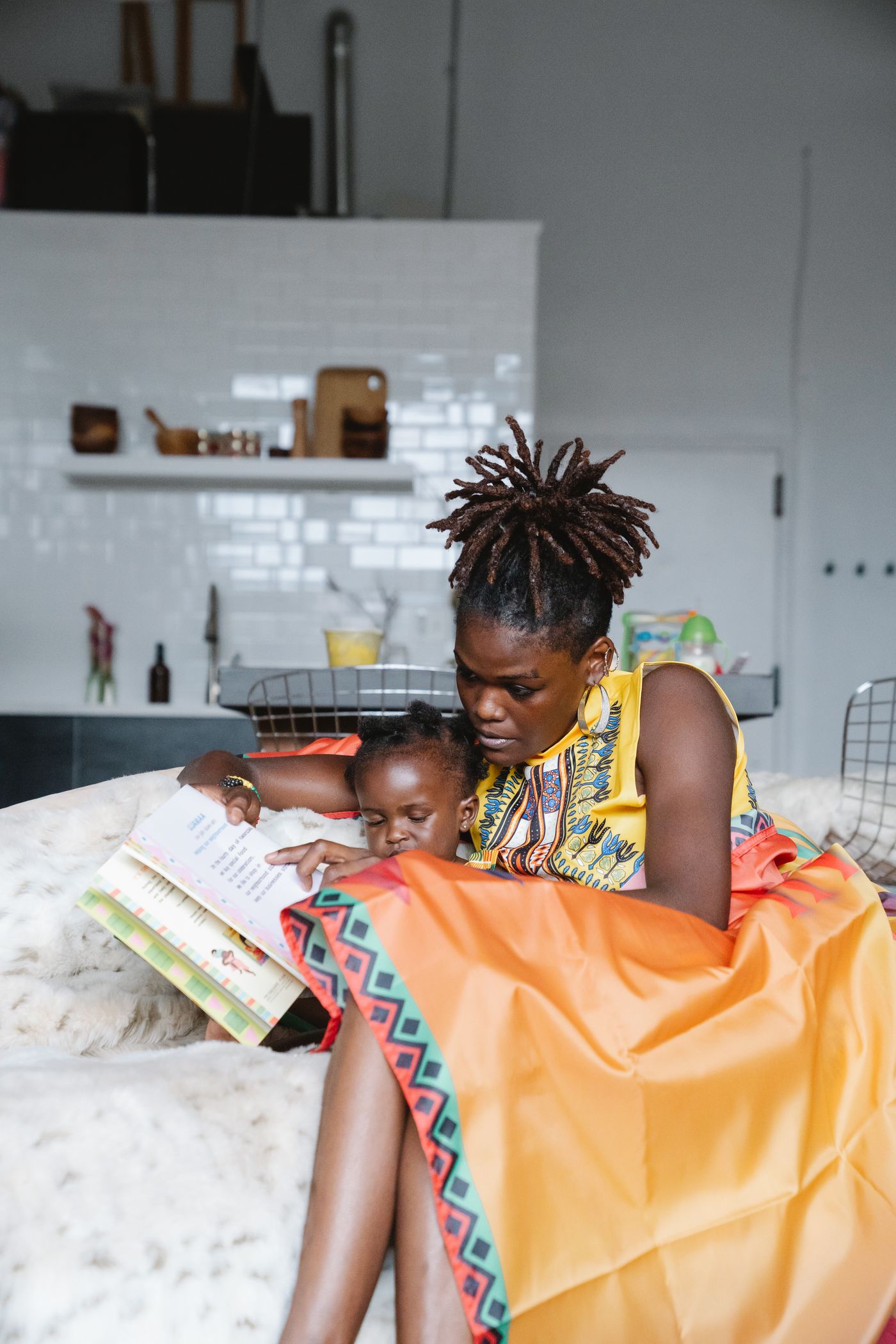 A mother and child sharing a book under an orange blanket