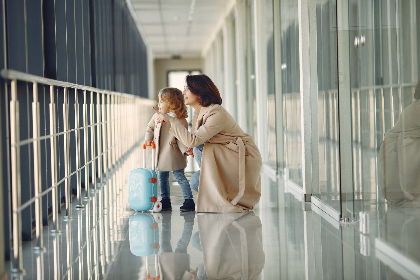 A woman and a child with luggage beside an airport window