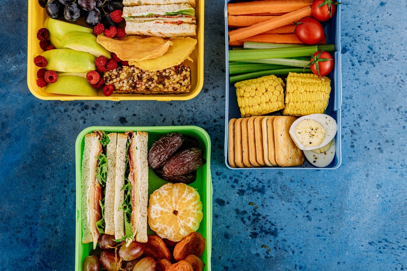 Three lunch boxes with sandwiches, fruit and vegetables