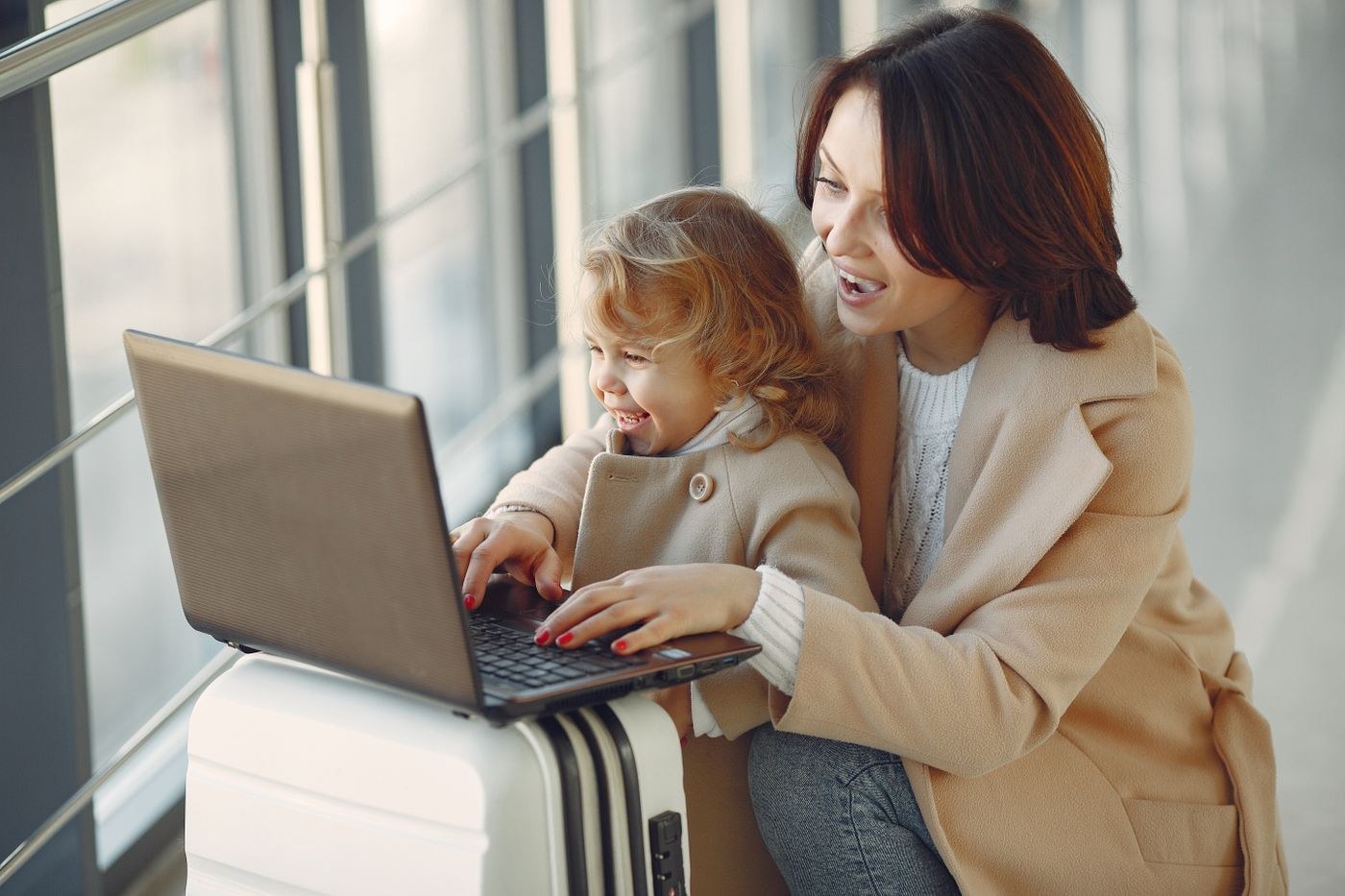 A woman and child looking at a laptop beside airport luggage