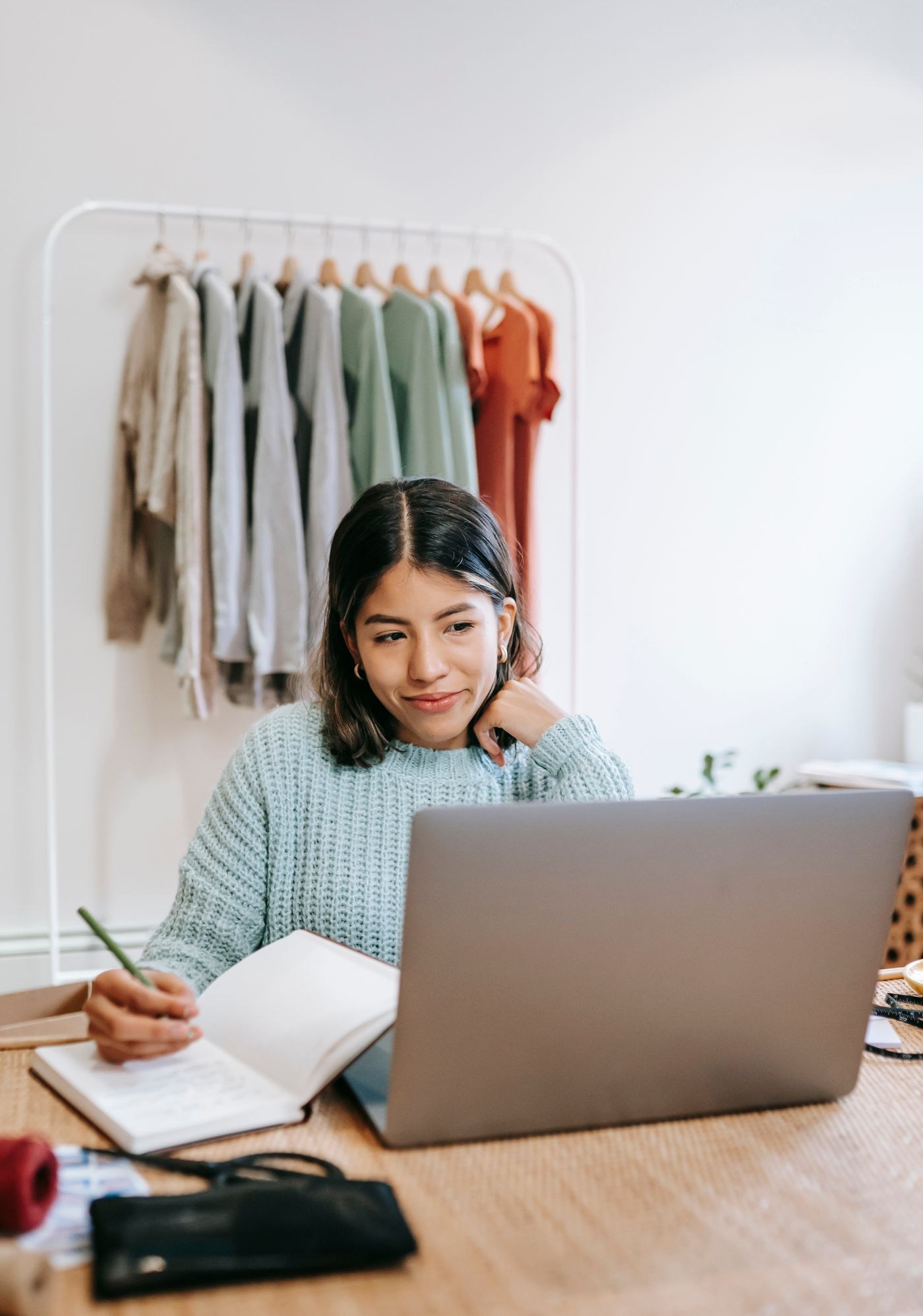 A woman using a laptop and writing in a notebook