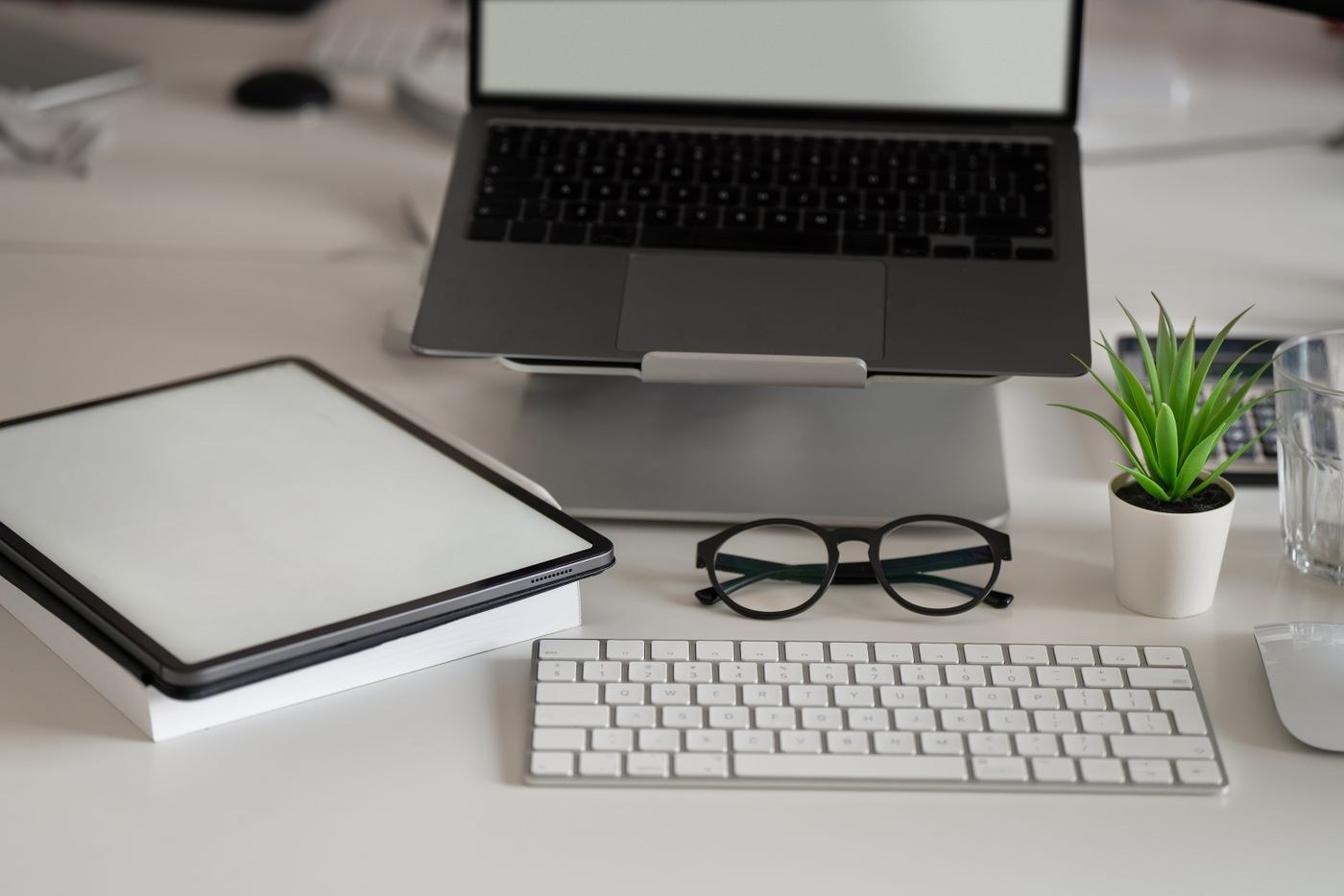 A laptop, keyboard and stationery on a desk